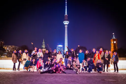 Gruppe von Teilnehmenden mit leuchtenden Funkkopfhörern posiert nachts vor dem Berliner Fernsehturm während einer Silent Disco Tour.