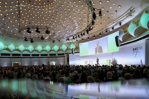 Großer Konferenzsaal mit Bühne, Redner und aufmerksamem Publikum, moderne Beleuchtung