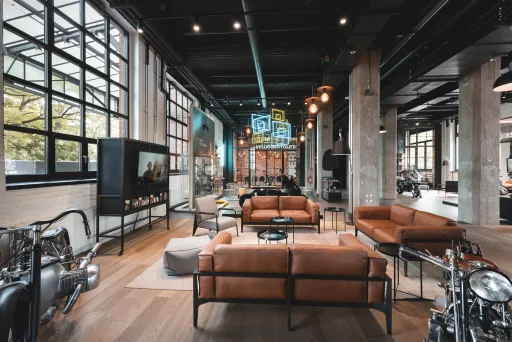 Moderner, heller Loftraum mit braunen Ledersofas, großen Fenstern und Industriecharakter.