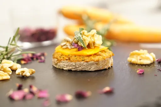 Rundstulle mit Aufstrich, Karotte und Walnuss auf schwarzem Teller, dekorativ angerichtet.