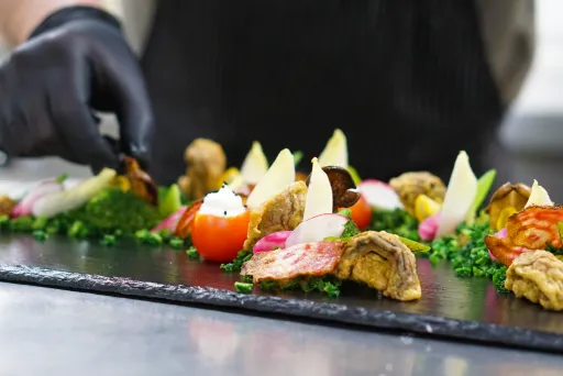 Koch arrangiert kunstvoll buntes Fingerfood auf schwarzer Platte.