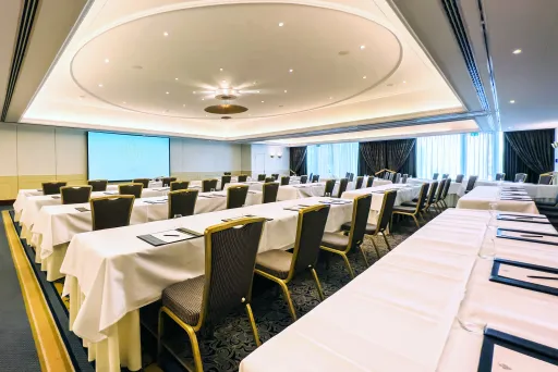 Tagungsraum mit langen, gedeckten Tischen und Stühlen, großer Bildschirm vorne