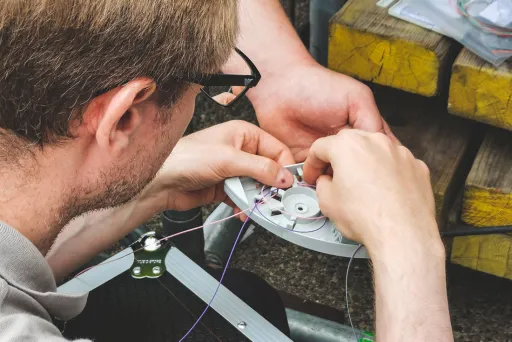 Mann repariert eine kleine mechanische Vorrichtung mit feinen Drähten.