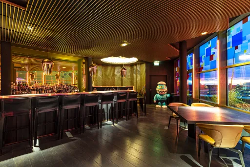 Moderne Bar mit goldener Decke, buntem Fenster und stilvollen Sitzbereichen.