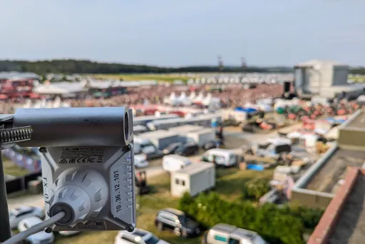 Überwachungskamera im Vordergrund, Festivalgelände mit Menschen im Hintergrund.