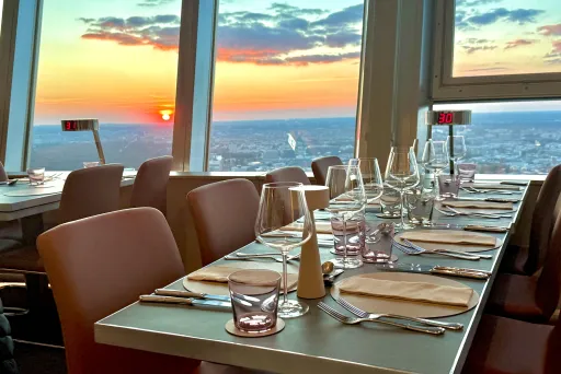 Gedeckter Restauranttisch am Fenster mit Blick auf Sonnenuntergang über der Stadt.