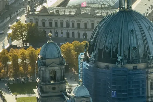 Berliner Dom mit Kuppel im Sonnenlicht, umgeben von Bäumen und Gebäuden.