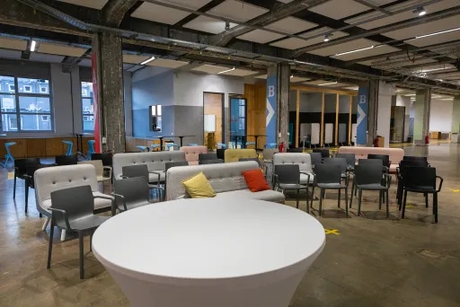 Moderner Veranstaltungsraum mit Stühlen, Sofas und runden Tischen, bunte Kissen.