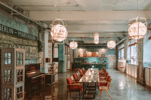 Moderner, industrieller Besprechungsraum mit langen Tischen, roten Stühlen und großen Lampen.