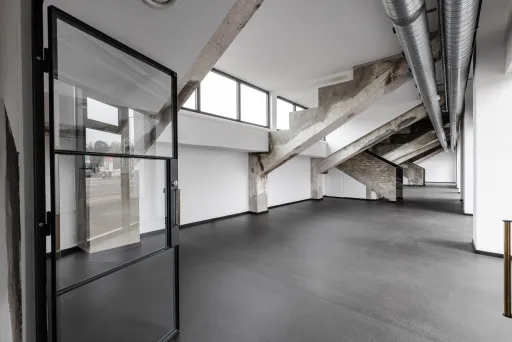 Leerer, moderner Raum mit großen Fenstern, Betonstützen und grauem Boden.