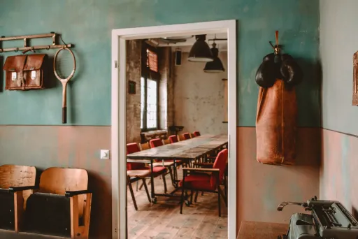 Tisch mit roten Stühlen in einem vintage Raum, Boxsack und Tennisschläger an der Wand.