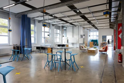 Heller, moderner Raum mit blauen Stühlen, Tischen und großen Fenstern