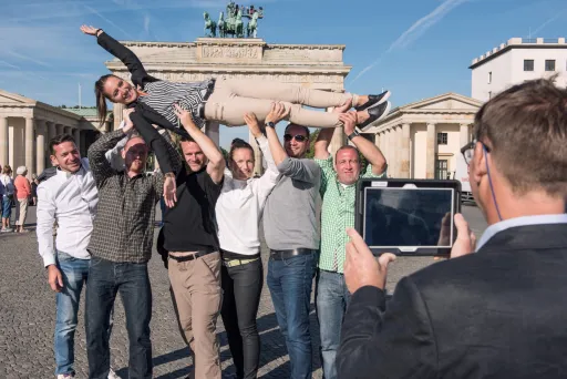 Gruppe fröhlicher Menschen posiert vor dem Brandenburger Tor für ein Foto.