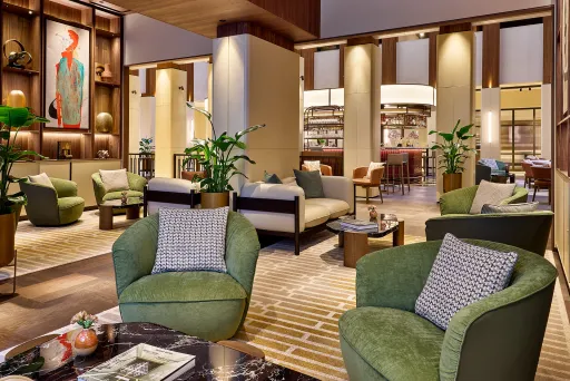 Modern eingerichtete Hotellobby mit grünen Sesseln, Pflanzen und warmem Licht.