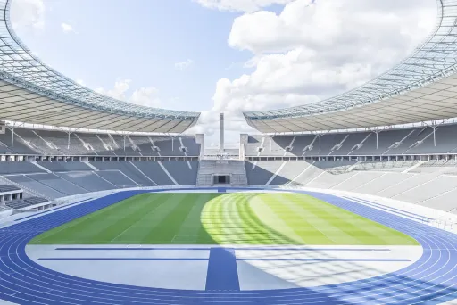 Innenraum des Olympiastadions Berlin mit Tribünen, blauer Laufbahn und grünem Fußballrasen