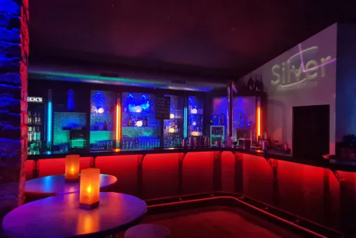 Stimmungsvolle Bar mit buntem Licht, leeren Tischen und Kerzen.