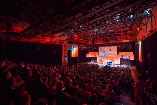 Großer Konferenzsaal mit gefüllten Sitzreihen und beleuchteter Bühne.