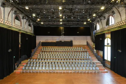 Leerer Veranstaltungssaal mit vielen Stuhlreihen und großer Bühne.