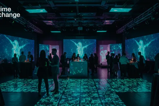 Menschen bei einer Veranstaltung in einem dunklen Raum mit blau beleuchteten Projektionen.