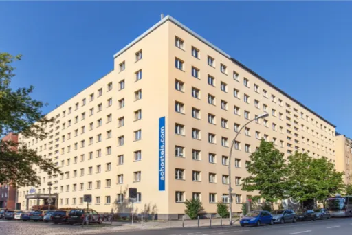 Großes, beiges Hotelgebäude mit mehreren Stockwerken an einer Straßenecke bei Sonnenschein.