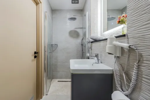 Modernes, schmales Badezimmer mit Dusche, Waschbecken, Spiegel und Föhn an der Wand.