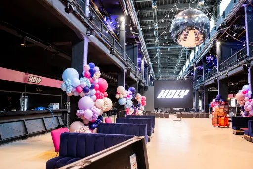 Große Eventhalle mit bunten Ballons, Sofas und einer Diskokugel an der Decke.