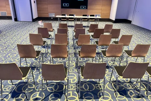 Leerer Konferenzraum mit Reihen von Stühlen und einem Tisch vorne.
