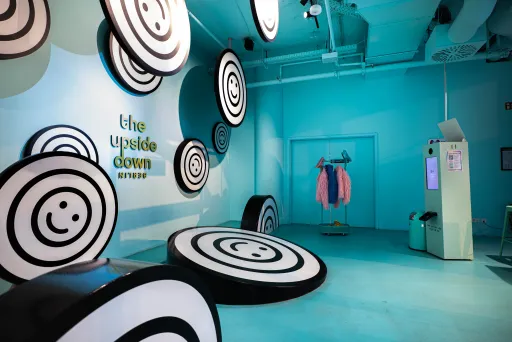 Raum mit blauen Wänden, schwarz-weißen Kreisen und einer rosa Jacke auf einem Kleiderständer.