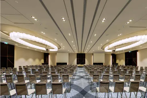 Großer, leerer Konferenzraum mit vielen aufgereihten Stühlen und moderner Beleuchtung.
