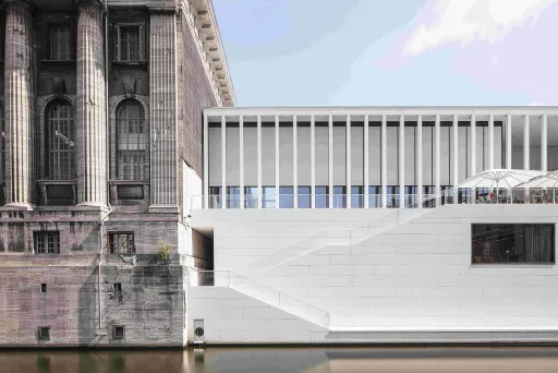 Altes Steingebäude neben modernem weißen Bau am Wasser.