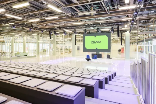 Heller, moderner Konferenzsaal mit großen Sitzstufen und einer Bühne samt Leinwand.