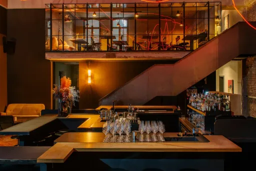Moderne Bar mit dunkler Einrichtung, leeren Hockern und roten Lichtlinien an der Decke.