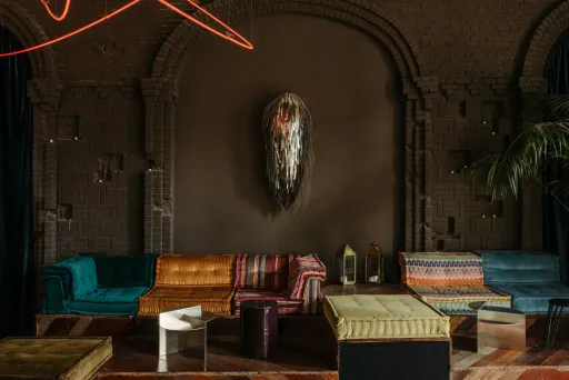 Bunte Sofas und Tische vor dunkelbrauner Wand mit Kunstwerk, warme gemütliche Atmosphäre.