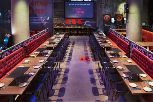 Modernes Restaurant mit langen Holztischen, roten Polsterbänken und dunklem Ambiente.