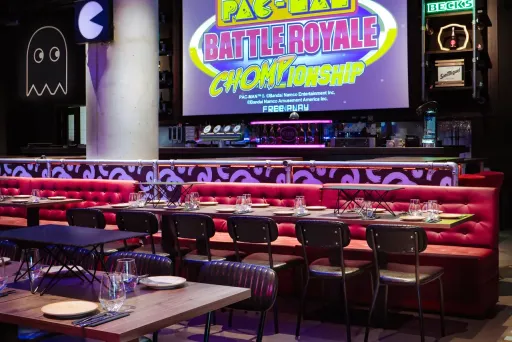 Modernes Restaurant mit roten Sitzbänken und großem Pac-Man-Spiele-Screen an der Wand.