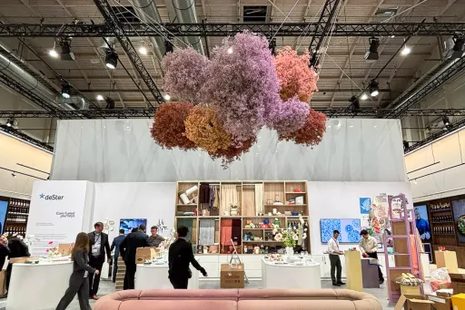 Moderne Messehalle mit beiger Couch und schwebender Blumendekoration in Rosa und Orange.
