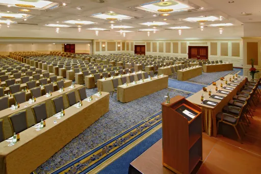 Großer Konferenzsaal mit vielen leeren Tischen und Stühlen, Rednerpult im Vordergrund.
