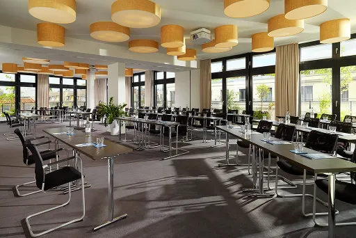 Heller Konferenzraum mit vielen Tischen, Stühlen und großen Fenstern
