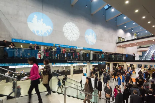 Viele Menschen in einer modernen Messehalle mit Projektionen an der Wand.