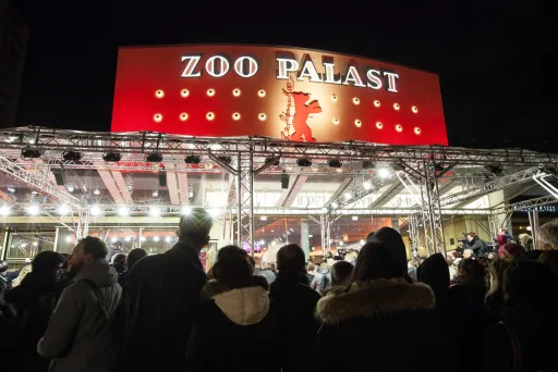 Menschenmenge vor dem beleuchteten Kino Zoo Palast bei Nacht.