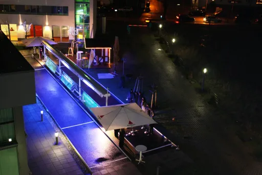 Beleuchtete Terrasse mit Sonnenschirmen und blau-violettem Licht bei Nacht