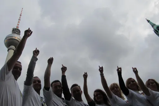 Gruppe von Menschen zeigt nach oben, Fernsehturm im Hintergrund, bewölkter Himmel.