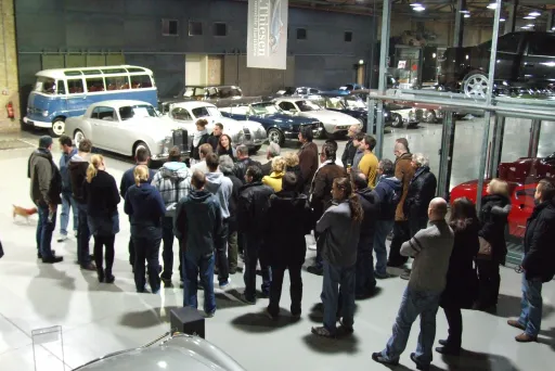 Gruppe Menschen in einer Oldtimerausstellung, umgeben von klassischen Autos.