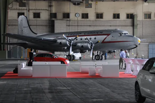 Silbernes Flugzeug in Hangar, rote Teppichfläche mit Autos und Stehtischen davor
