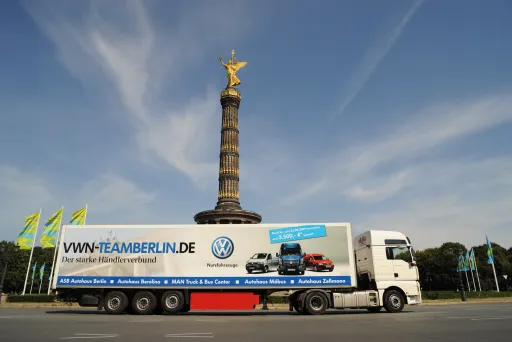 LKW vor der Berliner Siegessäule bei blauem Himmel, Werbeaufschrift am LKW.