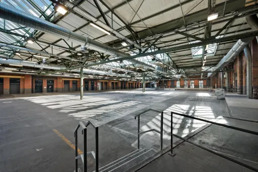 Leere Industriehalle mit Stahlträgern und Oberlichtern, viel Tageslicht.