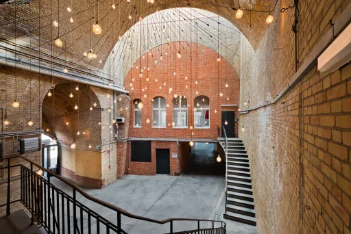 Großer Backsteinraum mit Gewölbedecke, Hängelampen und breiter Treppe.