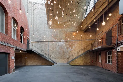 Innenhof mit Backsteinwänden, Treppen und vielen hängenden Glühbirnen