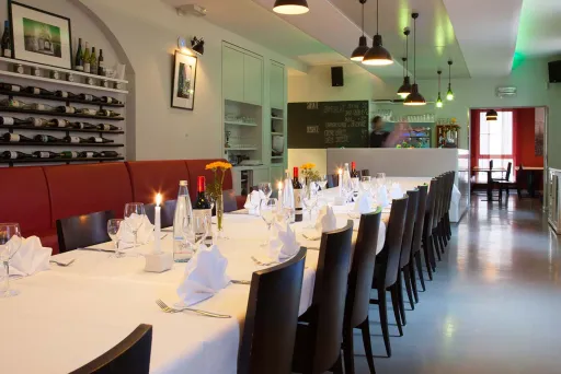 Langer, festlich gedeckter Tisch in modernem Restaurant mit Kerzen und Weingläsern.