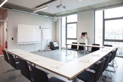 Heller Konferenzraum mit U-förmigem Tisch, Stühlen und Whiteboard.